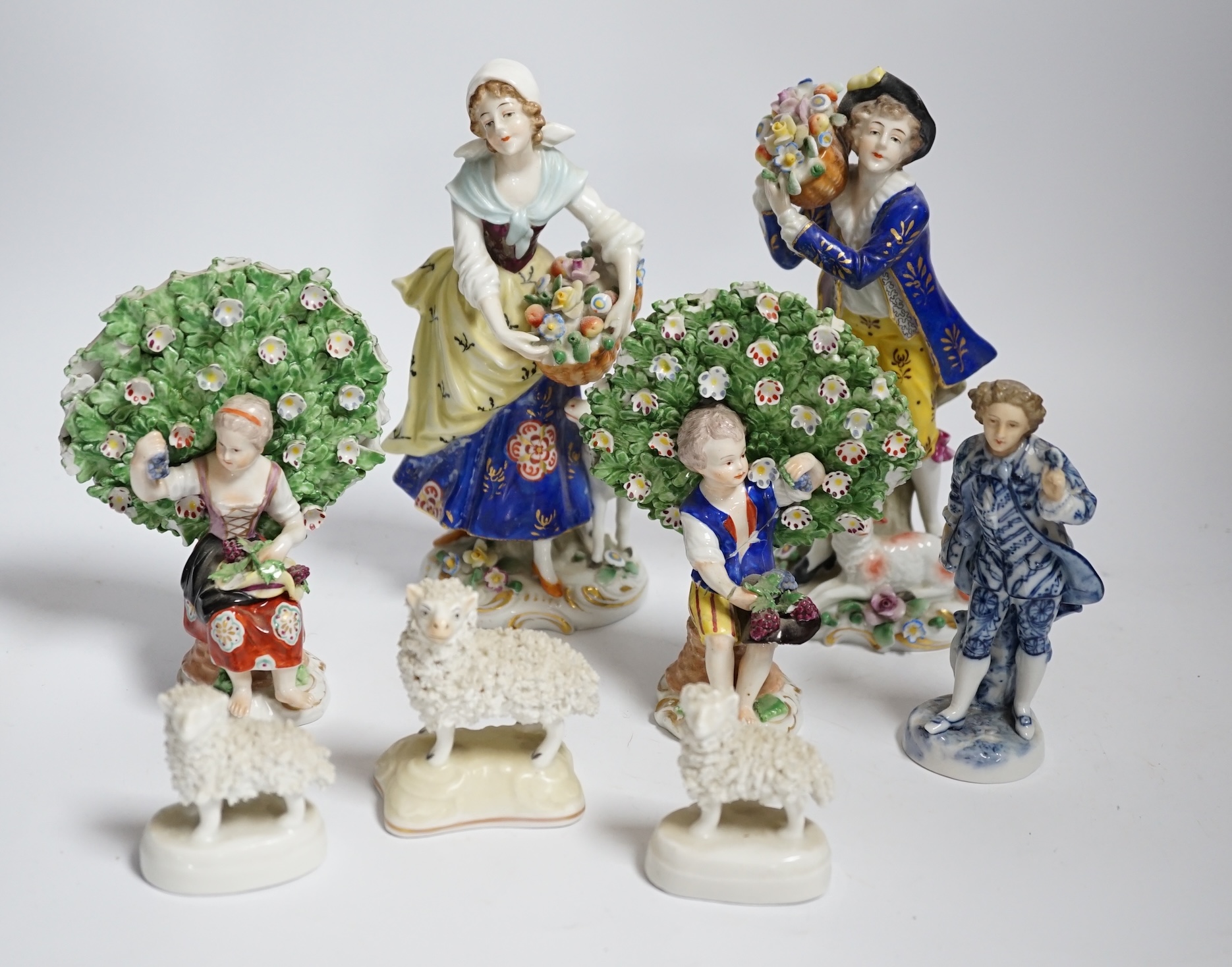 A pair of Derby style porcelain small bocage figures, a boy and girl seated with grape filled hats, height 14cm, three porcelain lambs and another figure